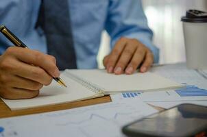 Businessman using pen writing note book planning journal and analysis information statistics document on desk. photo