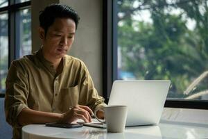 man asian working laptop computer and smartphone on desk focused on his work, with a serious expression on his face. photo