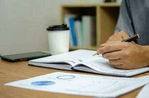Businessman using pen writing note book planning journal and analysis information statistics document on desk. photo