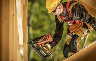 Construction Worker with a Nail Gun Assembling Wooden Skeleton Frame Beams photo