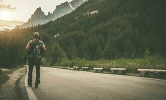 Photographer with Camera and Tripod Walking Along Mountain Road photo