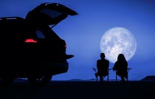 Couple Seating Next to Their Vehicle and Enjoying Full Moon Vista photo