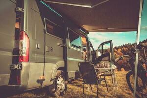 Life on the Move. Sunny Autumn Day. Family Camper Parked in a Scenic Spot in Front of a Forest. Break from Cycling to Play Chess. Travel Theme. photo