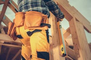 Contractor Using Spirit Level While Building Wooden House Frame photo