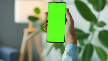 Woman at home using smartphone with green mock-up screen in vertical mode. Girl browsing Internet, watching content video