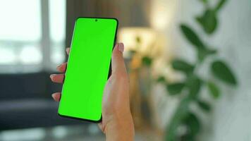 Woman at home using smartphone with green mock-up screen in vertical mode. Girl browsing Internet, watching content video