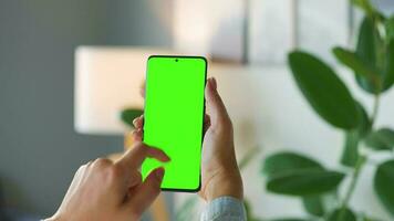 Woman at home using smartphone with green mock-up screen in vertical mode. Girl browsing Internet, watching content video