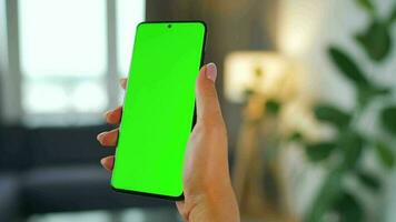 Woman at home using smartphone with green mock-up screen in vertical mode. Girl browsing Internet, watching content video