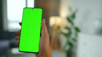 Woman at home using smartphone with green mock-up screen in vertical mode. Girl browsing Internet, watching content video