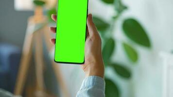 Woman at home using smartphone with green mock-up screen in vertical mode. Girl browsing Internet, watching content video