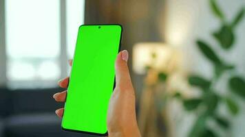 Woman at home using smartphone with green mock-up screen in vertical mode. Girl browsing Internet, watching content video