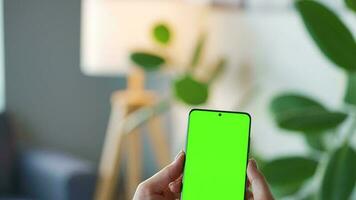 Woman at home using smartphone with green mock-up screen in vertical mode. Girl browsing Internet, watching content video