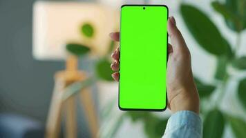 vrouw Bij huis gebruik makend van smartphone met groen mock-up scherm in verticaal modus. meisje browsen internetten, aan het kijken inhoud video