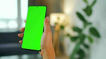 Woman at home using smartphone with green mock-up screen in vertical mode. Girl browsing Internet, watching content video