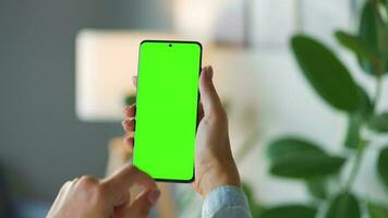 Woman at home using smartphone with green mock-up screen in vertical mode. Girl browsing Internet, watching content video