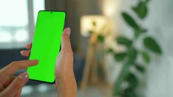 Woman at home using smartphone with green mock-up screen in vertical mode. Girl browsing Internet, watching content video