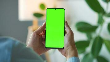 Woman at home using smartphone with green mock-up screen in vertical mode. Girl browsing Internet, watching content video