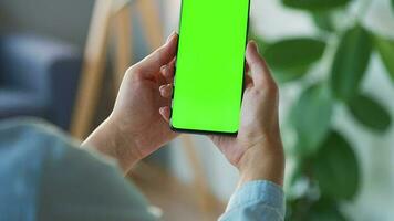 kvinna på Hem använder sig av smartphone med grön mock-up skärm i vertikal läge. flicka bläddring internet, tittar på innehåll video