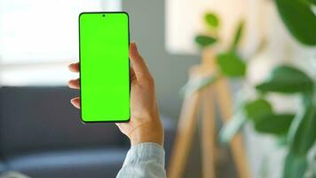 Woman at home using smartphone with green mock-up screen in vertical mode. Girl browsing Internet, watching content video