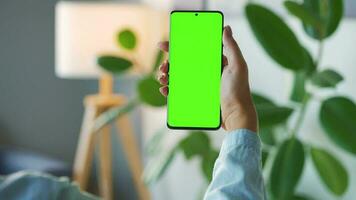 Woman at home using smartphone with green mock-up screen in vertical mode. Girl browsing Internet, watching content video