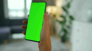 donna a casa utilizzando smartphone con verde modello schermo nel verticale modalità. ragazza navigazione Internet, Guardando soddisfare video