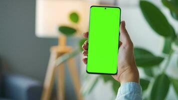 vrouw Bij huis gebruik makend van smartphone met groen mock-up scherm in verticaal modus. meisje browsen internetten, aan het kijken inhoud video