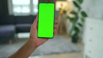 Woman at home using smartphone with green mock-up screen in vertical mode. Girl browsing Internet, watching content video