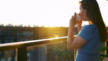 vrouw met een kop van koffie staand Aan de balkon en bewonderen de zonsondergang video