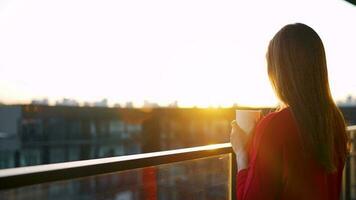 mujer con un taza de café en pie en el balcón y admirar el puesta de sol video