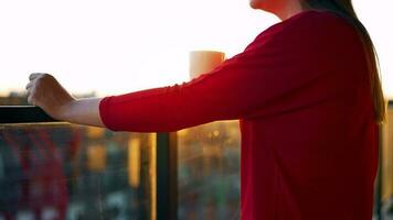 mujer con un taza de café en pie en el balcón y admirar el puesta de sol video