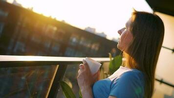 vrouw met een kop van koffie staand Aan de balkon en bewonderen de zonsondergang video