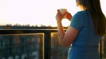 mujer con un taza de café en pie en el balcón y admirar el puesta de sol video
