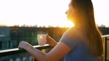 mujer con un taza de café en pie en el balcón y admirar el puesta de sol video