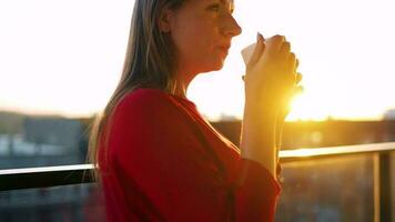 Frau mit ein Tasse von Kaffee Stehen auf das Balkon und bewundern das Sonnenuntergang video