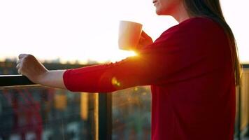 mulher com uma copo do café em pé em a sacada e admirar a pôr do sol video