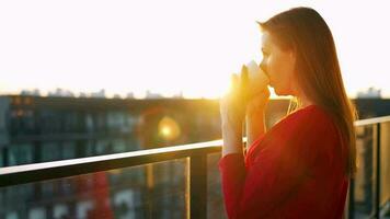 vrouw met een kop van koffie staand Aan de balkon en bewonderen de zonsondergang video