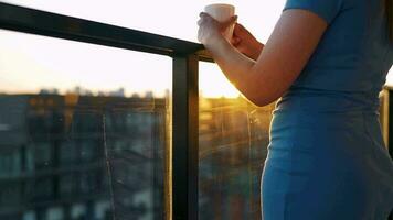 vrouw met een kop van koffie staand Aan de balkon en bewonderen de zonsondergang video