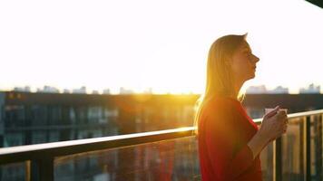 mujer con un taza de café en pie en el balcón y admirar el puesta de sol video