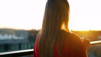 donna con un' tazza di caffè in piedi su il balcone e ammirare il tramonto video