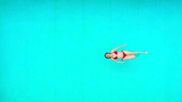 View from the top as a woman in red swimsuit lying on her back in the pool. Relaxing concept video