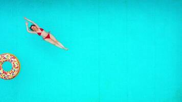 View from the top as a woman in red swimsuit lying on her back in the pool. Relaxing concept video