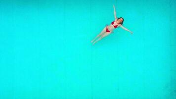 View from the top as a woman in red swimsuit lying on her back in the pool. Relaxing concept video