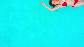 View from the top as a woman in red swimsuit lying on her back in the pool. Relaxing concept video