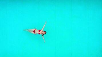 View from the top as a woman in red swimsuit lying on her back in the pool. Relaxing concept video