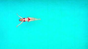 visie van de top net zo een vrouw in rood zwempak aan het liegen Aan haar terug in de zwembad. ontspannende concept video