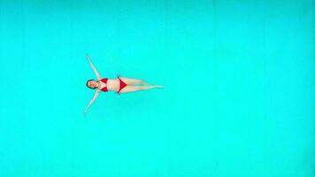 View from the top as a woman in red swimsuit lying on her back in the pool. Relaxing concept video