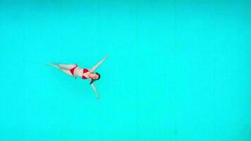 View from the top as a woman in red swimsuit lying on her back in the pool. Relaxing concept video