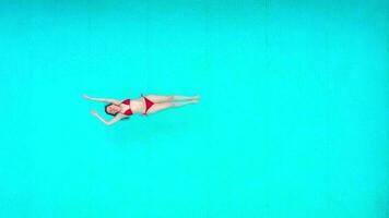vue de le Haut comme une femme dans rouge maillot de bain mensonge sur sa retour dans le bassin. relaxant concept video