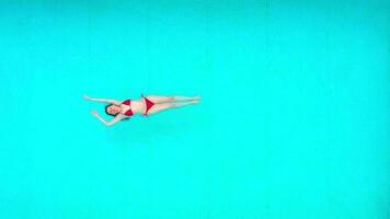 View from the top as a woman in red swimsuit lying on her back in the pool. Relaxing concept video