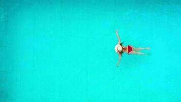 View from the top as a woman in red swimsuit lying on her back in the pool. Relaxing concept video